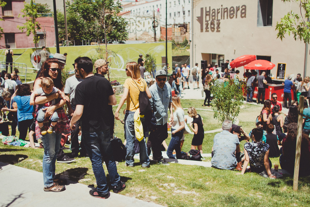 Fotografía de un parque en el que se ve mucha gente, al fondo se encuentra un edificio con el cartel de "Harinera ZGZ", también se aprecia una barra de bar dando a entender que es un evento festivo.